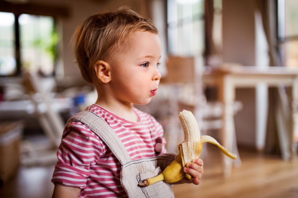 a small toddler girl indoors, eating banana fruit