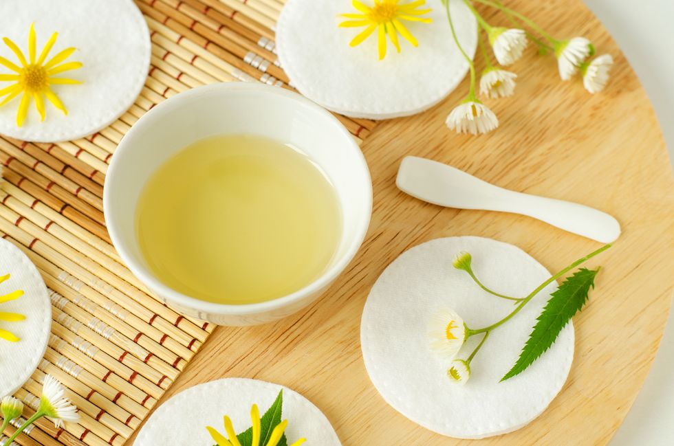 small white bowl with cosmetic massage, cleansing aroma oil, cotton pads and wild flowers natural skin care, homemade spa and beauty treatment recipe top view, copy space