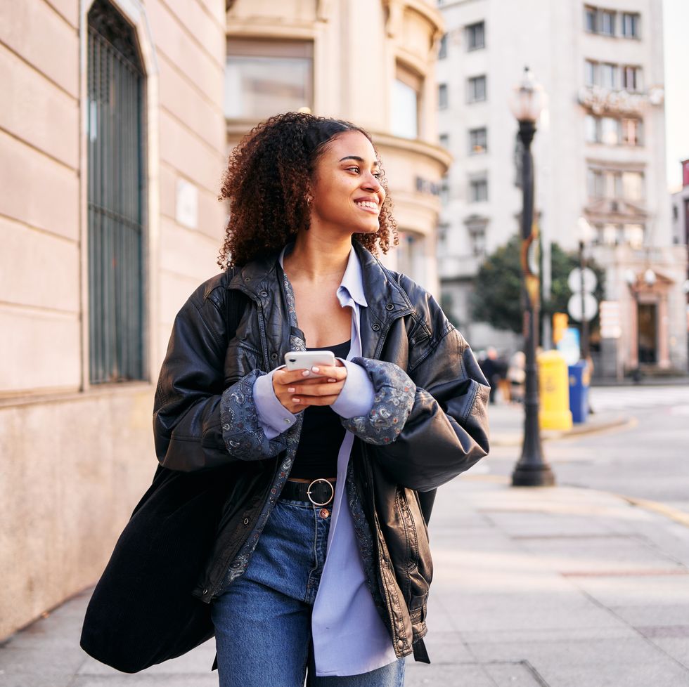 smiley afro woman using a mobile walking in the street