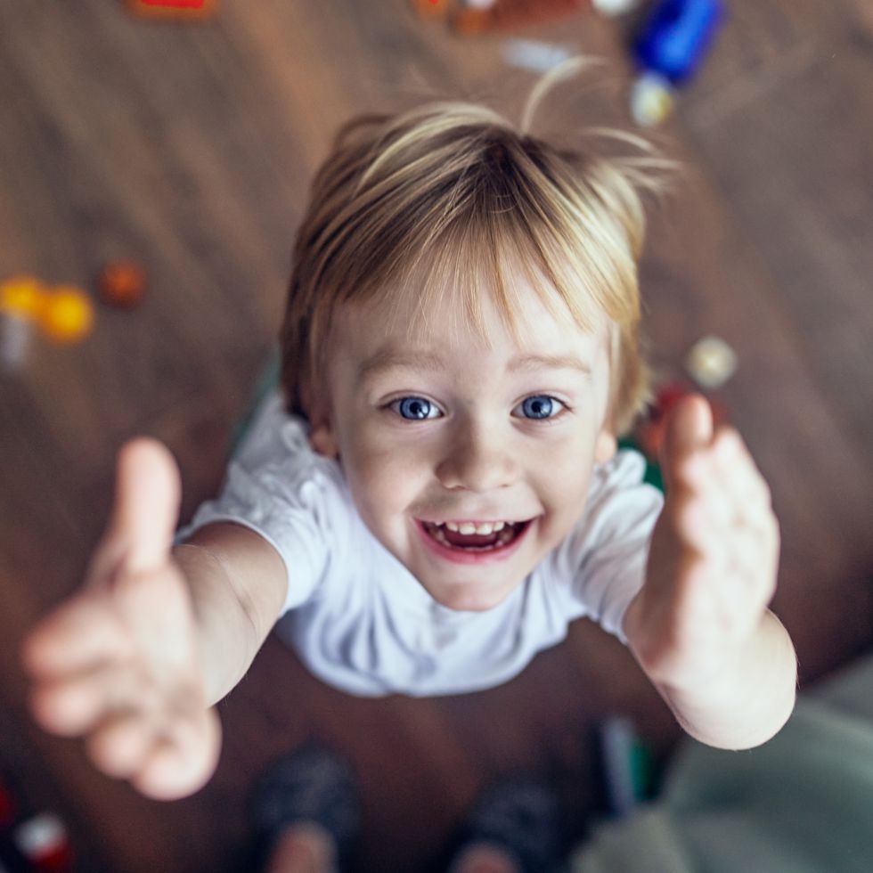 a smiling 3 year old boy jumps and raises his hands up and looks at the camera.