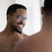smiling african american man in glasses look in bathroom mirror