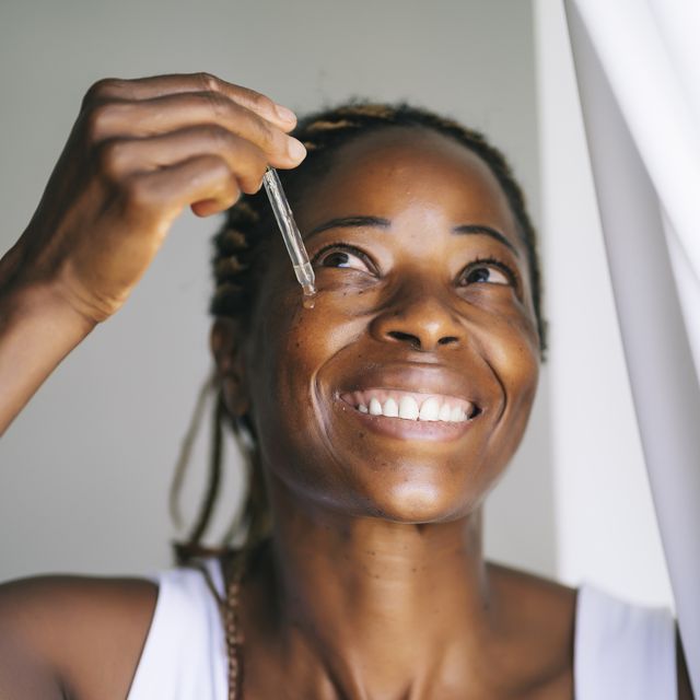 smiling afro woman looking up while applying face serum