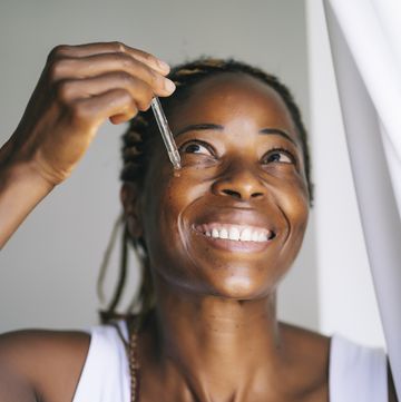 smiling afro woman looking up while applying face serum