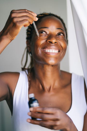 smiling afro woman looking up while applying face serum