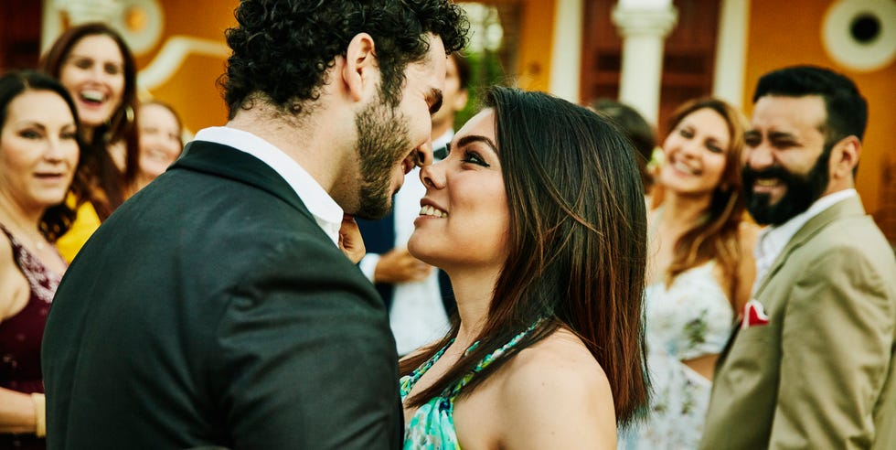 Pareja sonriente y abrazada a punto de besarse durante la recepción de la boda al aire libre sonriendo y abrazando a una pareja a punto de besarse durante la recepción de la boda al aire libre