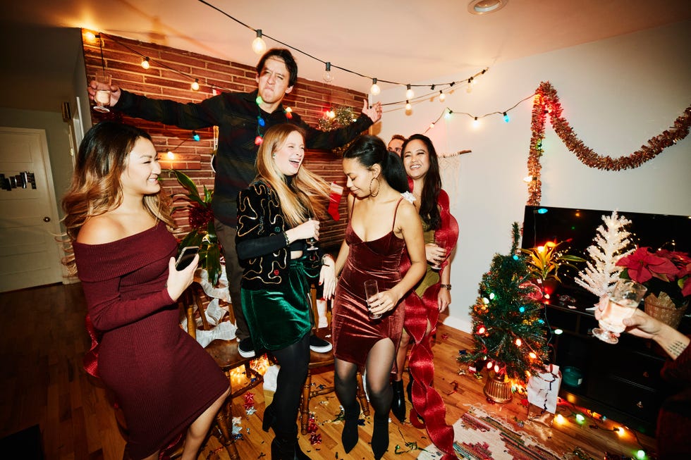 smiling and laughing friends dancing in living room during holiday party