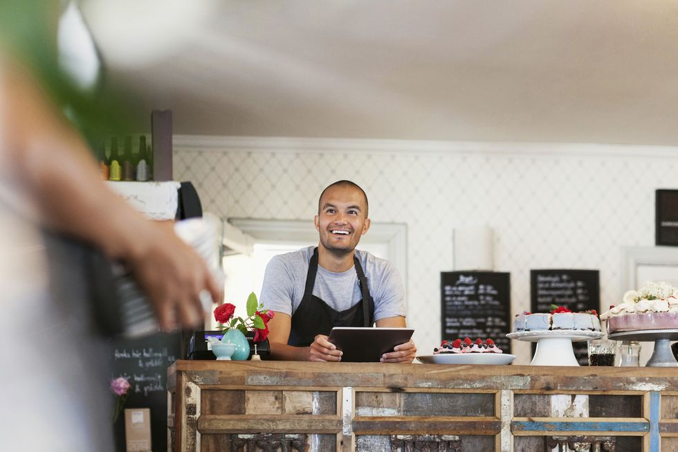 smiling baker holding digital tablet while looking at female colleague in cafe
