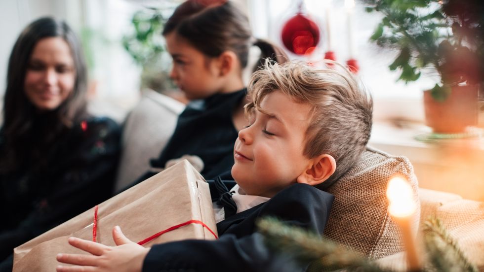 smiling boy holding christmas present while sitting with family in living room
