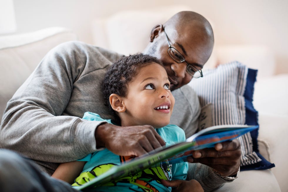 smiling boy looking at father while reading picture book at home