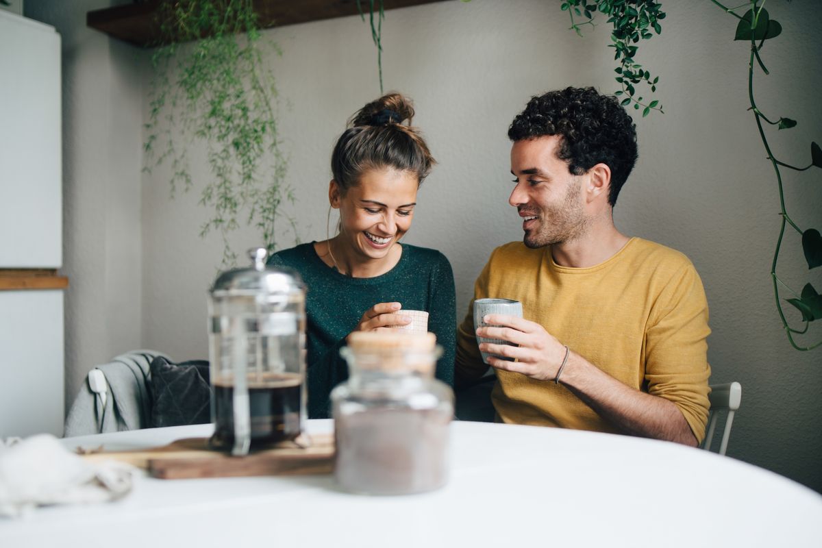smiling boyfriend and girlfriend having coffee at table in living room