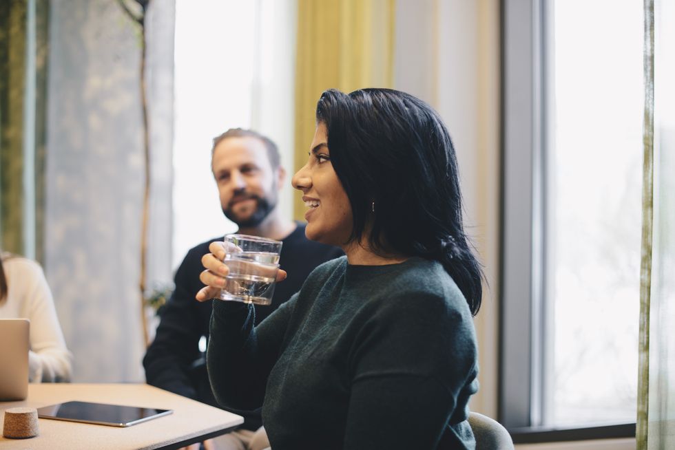 Smiling businesswoman holding glass of water while sitting at conference table with colleagues