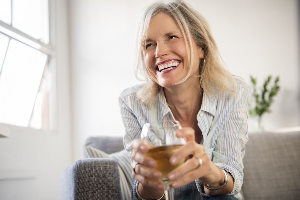 smiling caucasian woman sitting on sofa drinking white wine