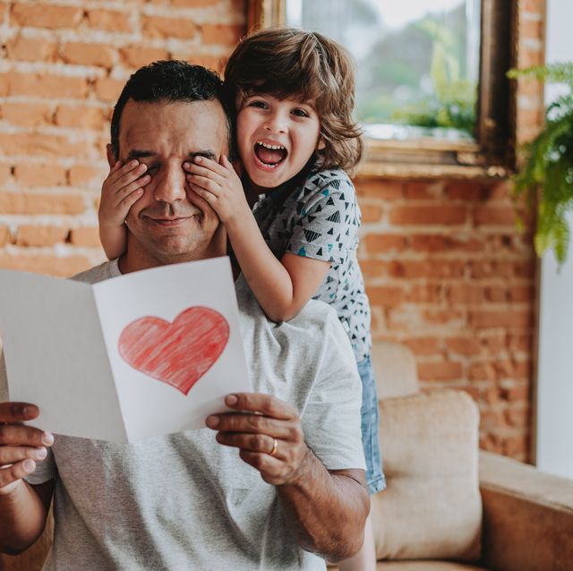 smiling child hiding father's eyes and handing gift postcard