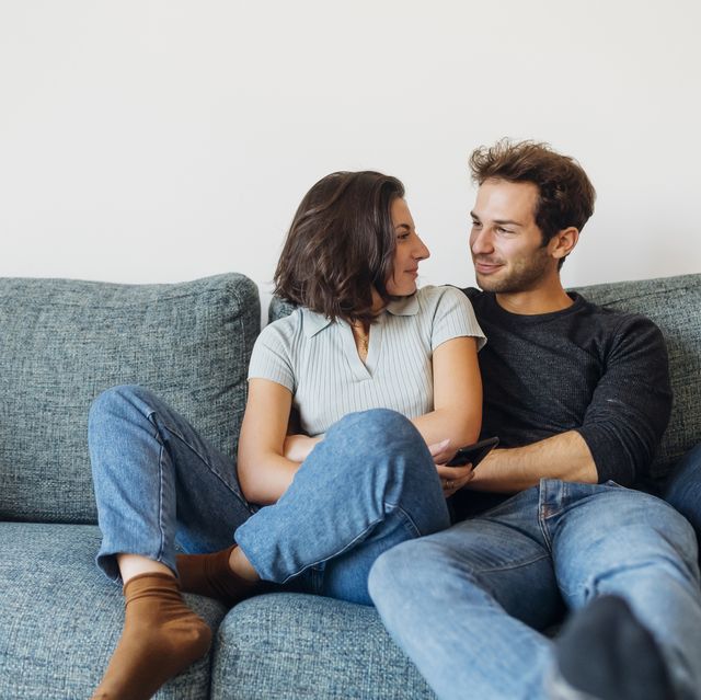 smiling couple looking at each other while sitting on sofa