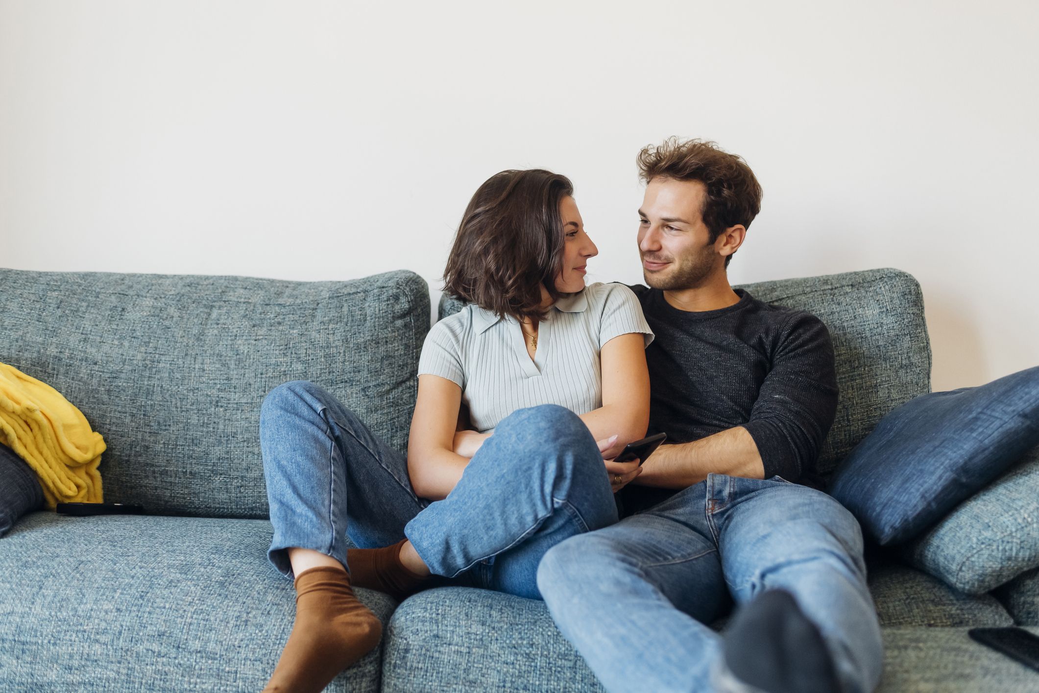 smiling couple looking at each other while sitting on sofa
