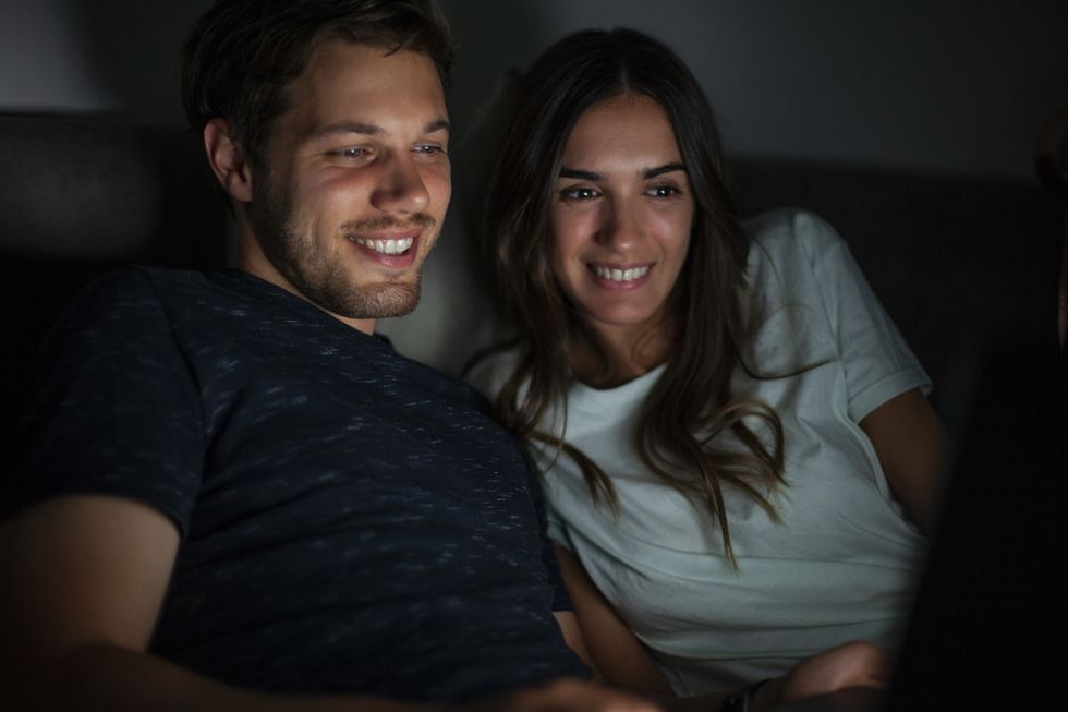 smiling couple lying on bed next to each other while watching online content during nightime