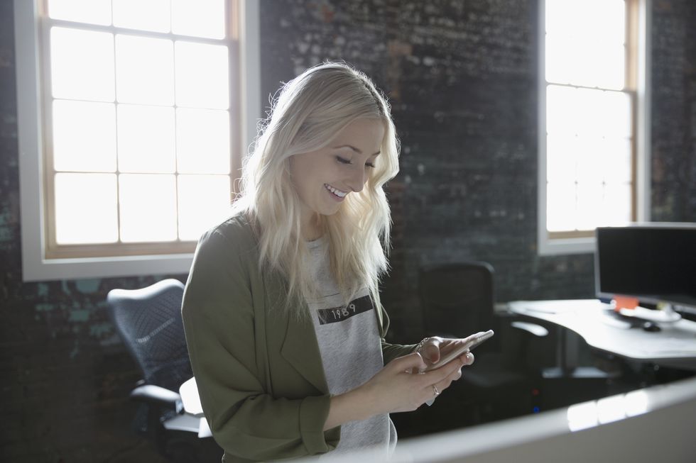 Smiling creative businesswoman texting with smart phone in office