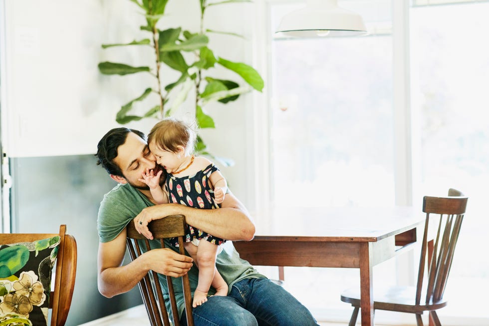 Smiling father holding and kissing infant daughter in dining room in home
