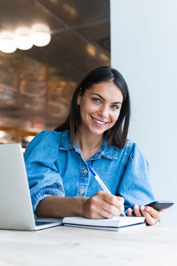 smiling female freelancer writing on diary at cafe