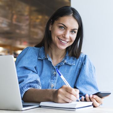 smiling female freelancer writing on diary at cafe