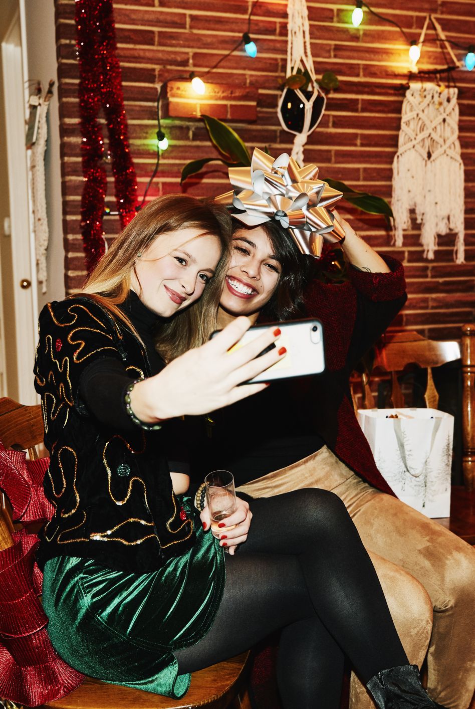 smiling female friends posing for selfie with bow over their heads during holiday party in home