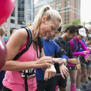 Smiling female marathon runner ready, preparing smart watch at starting line on urban street