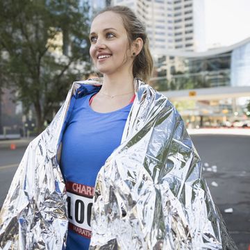 Smiling female marathon runner wrapped in thermal blanket