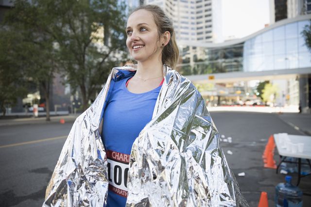 Smiling female marathon runner wrapped in thermal blanket