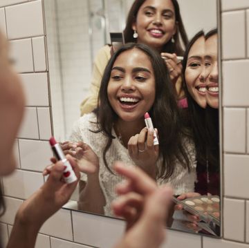 smiling friends with lipstick looking at mirror