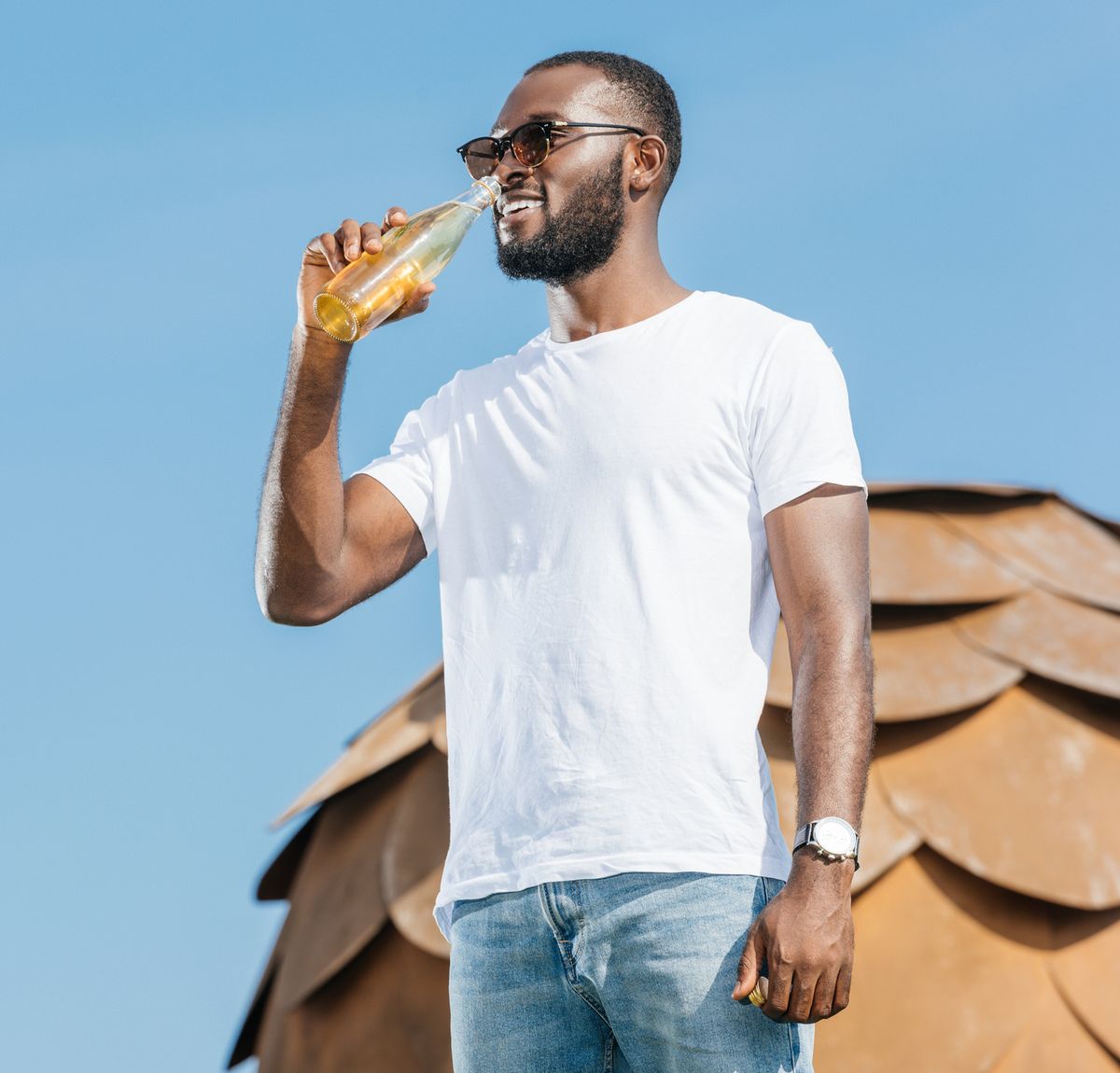 smiling handsome african american man drinking soda against blue sky