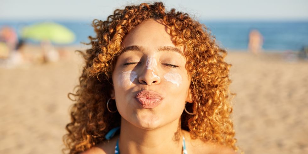 smiling happy woman applying sunscreen to her face on the beach at sunset