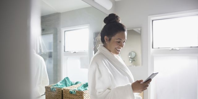 Smiling Latina woman using smart phone in bathroom