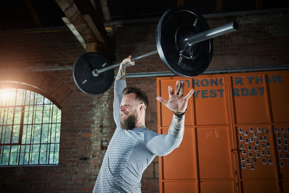 smiling male athlete lifting barbell at sports studio