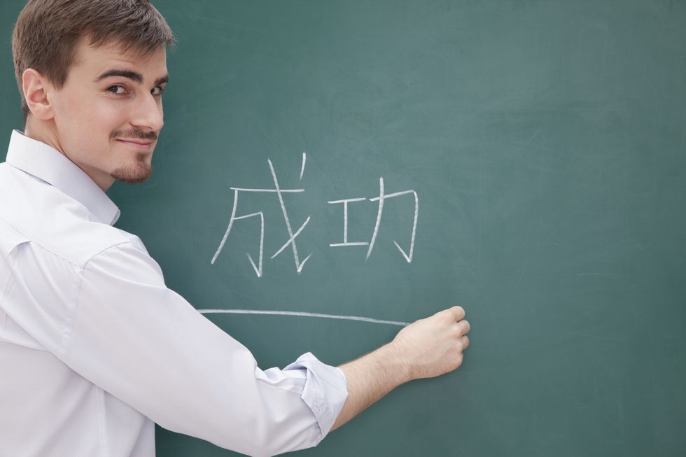 smiling male teacher in front of chalkboard writing, chinese characters