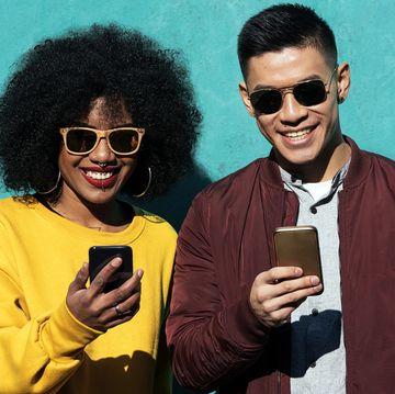 smiling man and woman using mobile phones while standing against turquoise wall