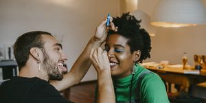 smiling man applying blue eyeliner to female friend at home