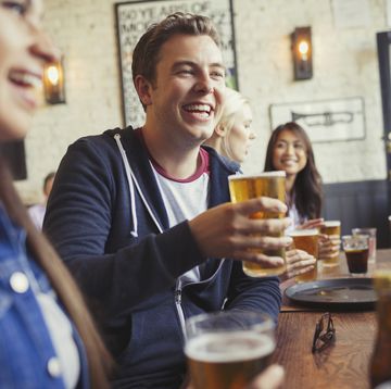 Smiling man drinking beer with friends at table in bar