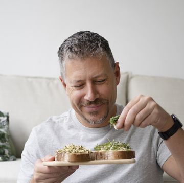 smiling man eating sprouts sitting in front of sofa at home