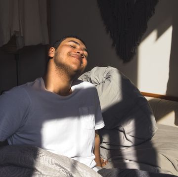 smiling man enjoying sunlight waking up in his bed at home
