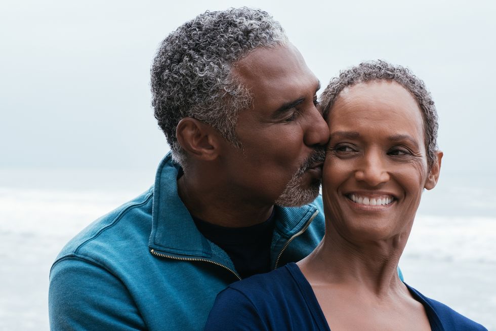 smiling man kissing wife on forehead at beach
