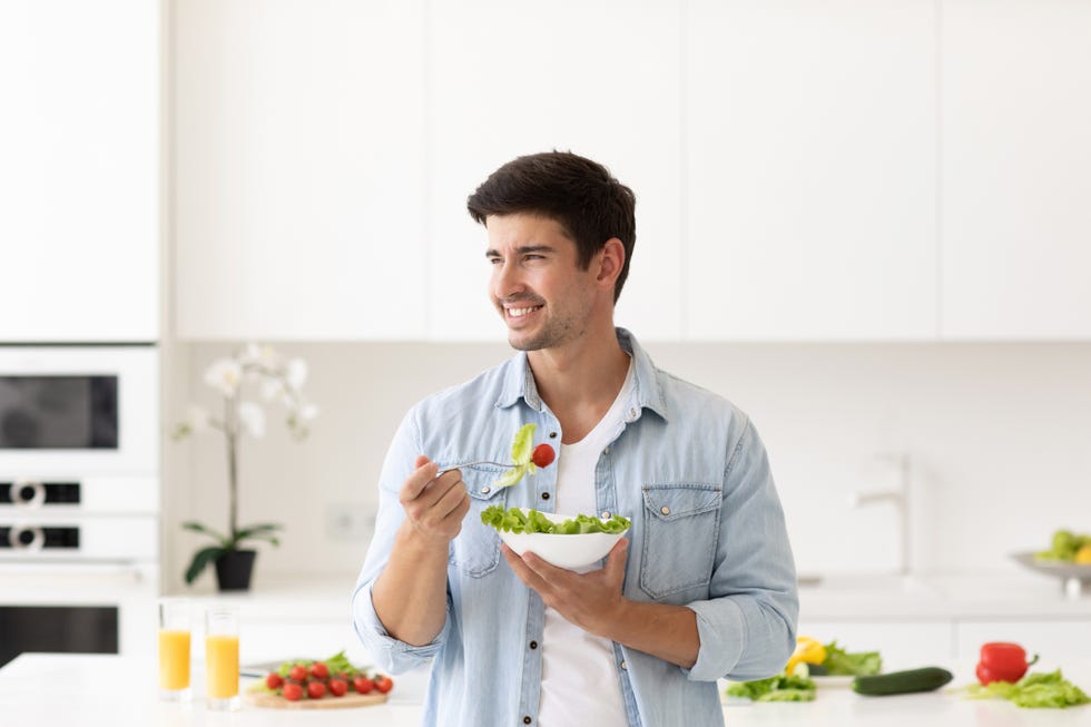 smiling man with plate of salad fresh vegetables on modern kitchen at home