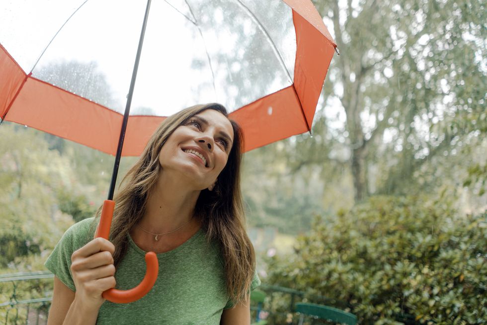 smiling mature woman standing in rain under umbrella