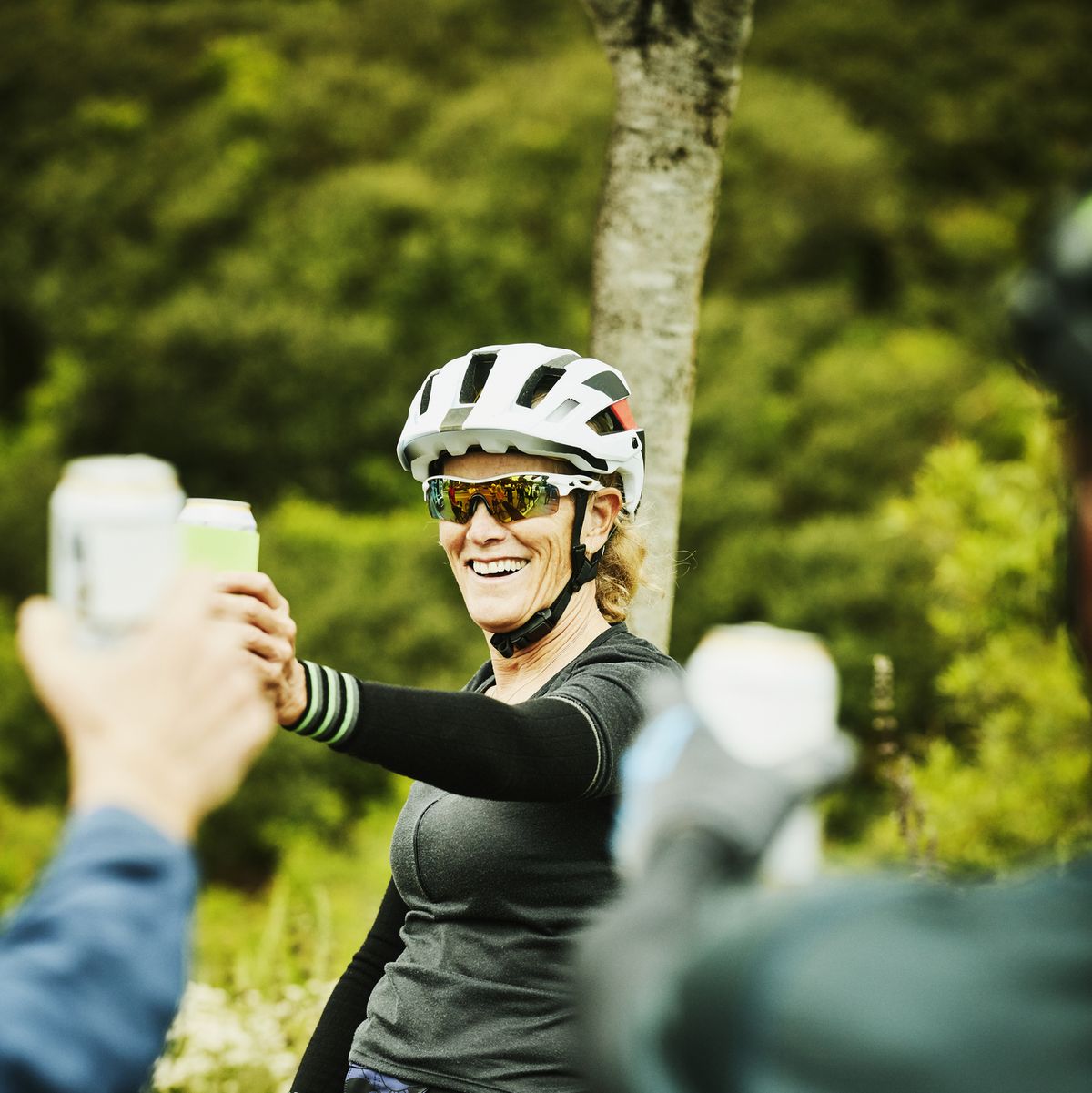 smiling mature woman toasting beers with friends after mountain bike ride