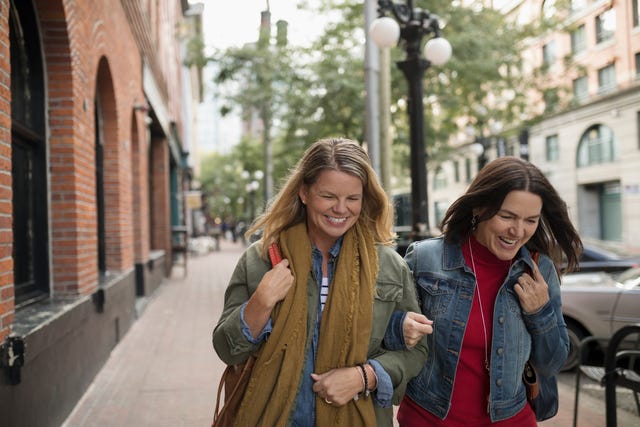 Smiling mature women friends walking arm in arm on urban sidewalk