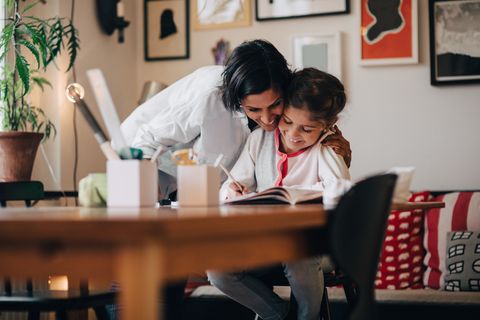 smiling mother embracing daughter studying on table at home