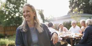 Smiling senior woman enjoying garden party lunch with friends on sunny patio