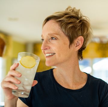 smiling stylish woman drinking a glass of water in her kitchen