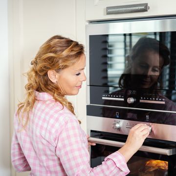 Smiling Woman Adjusting Heat Of Oven At Home