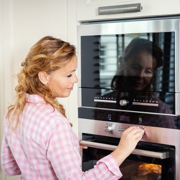 Smiling Woman Adjusting Heat Of Oven At Home