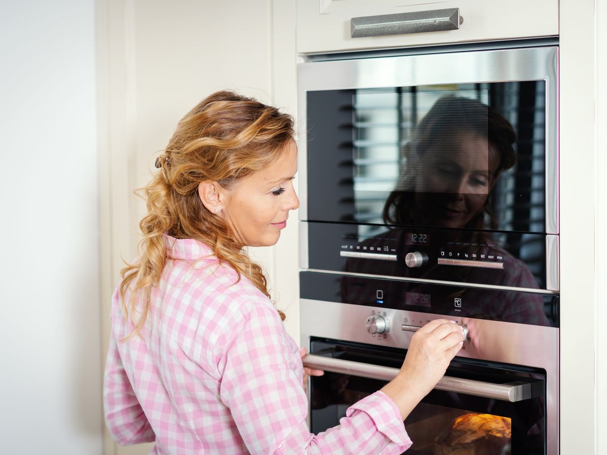 https://hips.hearstapps.com/hmg-prod/images/smiling-woman-adjusting-heat-of-oven-at-home-royalty-free-image-1582025768.jpg?crop=0.88889xw:1xh;center,top&resize=1200:*